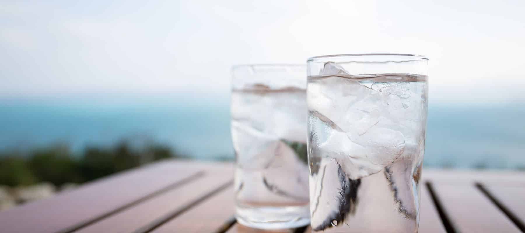 two glasses of water with ice sitting outside on a wooden table