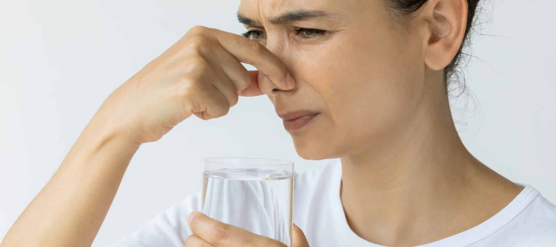 woman plugging her nose smelling bad odor on water in glass cup
