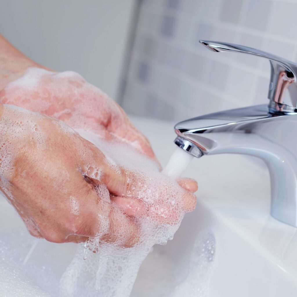 soapy hands washing under a stream of water coming from a bathroom faucet