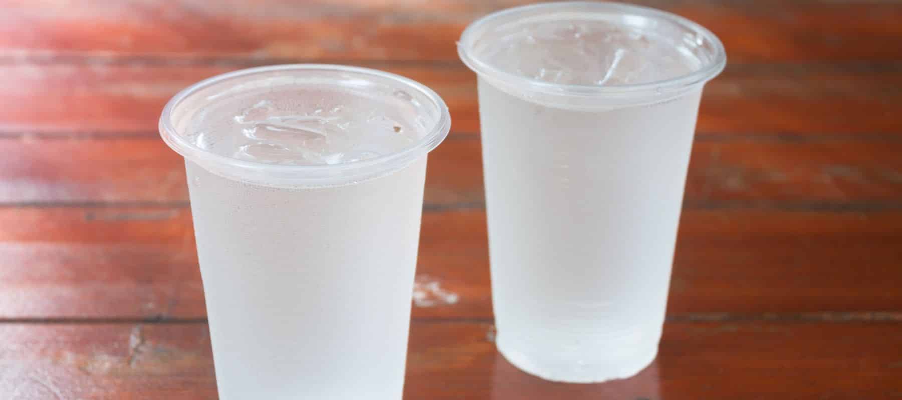 Two clear plastic cups filled with ice water sit on a wooden table, lightly covered in condensation
