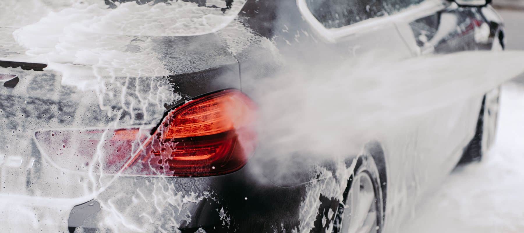 closeup of a black car covered in soap suds being sprayed by high water pressure car washer