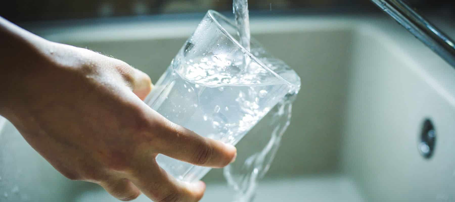 A person's hand holds a glass being filled with clear water from a faucet over a sink