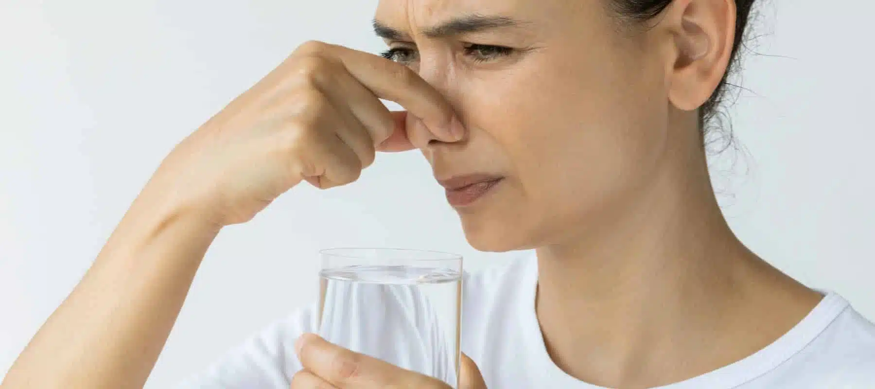 woman plugging her nose smelling bad odor on water in glass cup