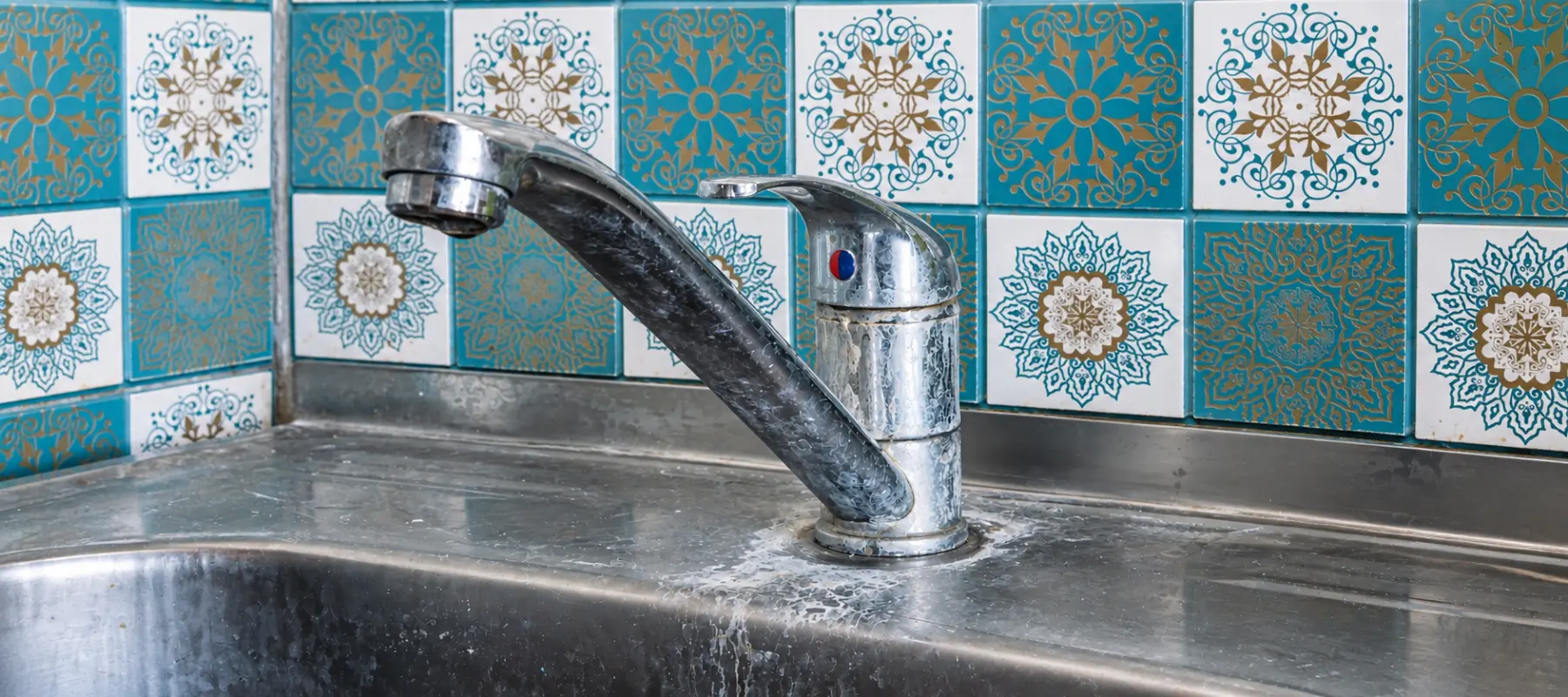 Hard water mineral buildup on a chrome faucet and stainless steel sink.